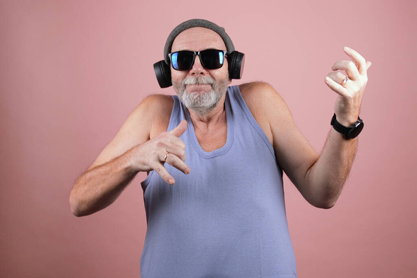 Хіпстер у віці чоловік у сірому капелюсі, блакитний бак, сонцезахисні окуляри та навушники енергійно грають на уявній гітарі. Приголомшливе соло на невидимій гітарі
 - Фото, зображення