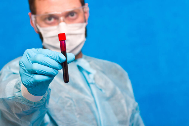 Male scientist holding test tube with blood on blue background. - Foto, afbeelding