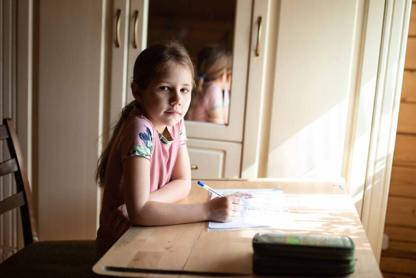 A little girl sitting on a table and doing homework - Foto, Bild