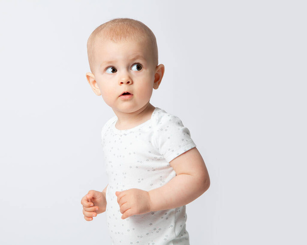 The European baby is surprised, looks up and away with his mouth open. Alertness. Children's emotions, spontaneity. Close-up, portrait of a child on a white background. - Фото, изображение