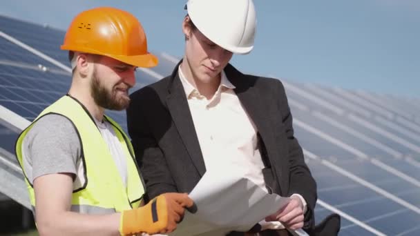 The businessman and worker are discussing documents standing near solar batteries outside - Filmati, video