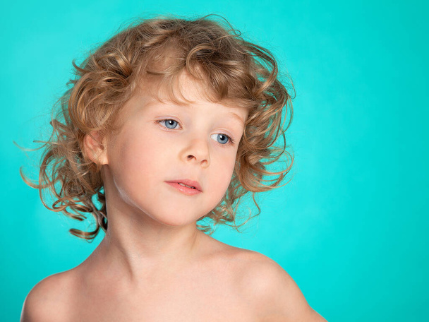 Portrait of a beautiful curly-haired boy with a European appearance on a background of sea-green. The blue-eyed four-year-old paused. Light sadness. Children are angels. - Foto, Imagen
