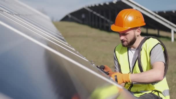 Mężczyzna inżynier w mundurze sprawdza baterię słoneczną na zewnątrz - Materiał filmowy, wideo