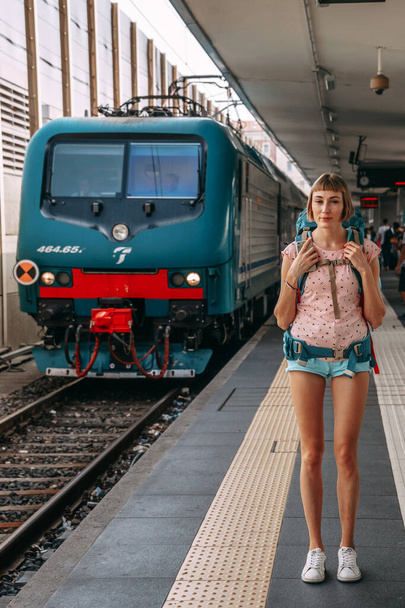 A girl with a backpack and shorts is waiting for the train to arrive at the railway station in Italy | BOLOGNA, ITALY - 17 SEPTEMBER 2018. - Photo, image