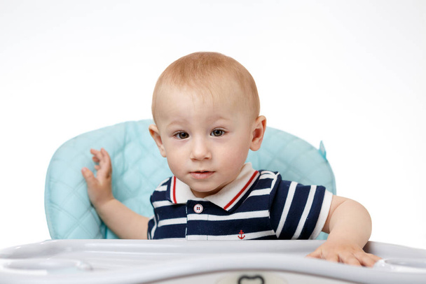 Cheerful little boy sitting in a child seat at the table on a white background - Photo, Image