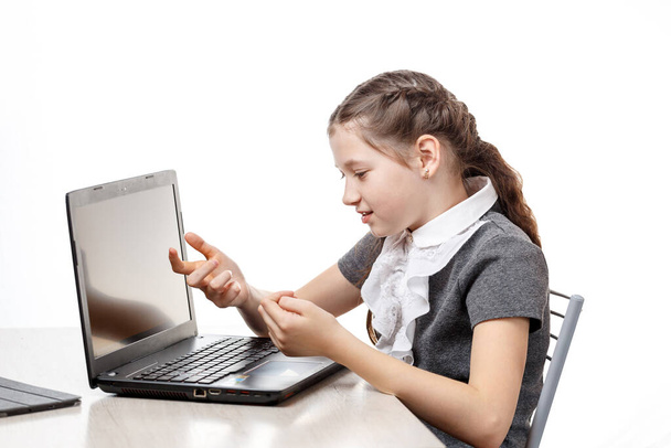 Cute schoolgirl sitting at a laptop on a white background - Fotó, kép