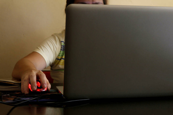 Photo of a Filipino woman's hand holding a computer mouse while working on a laptop computer at home. - Photo, Image