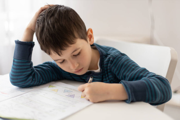 Porträt eines kleinen Jungen, der zu Hause mit seinen Hausaufgaben zu kämpfen hat. Bildungskonzept für Kinder zu Hause. Fernstudium - Foto, Bild