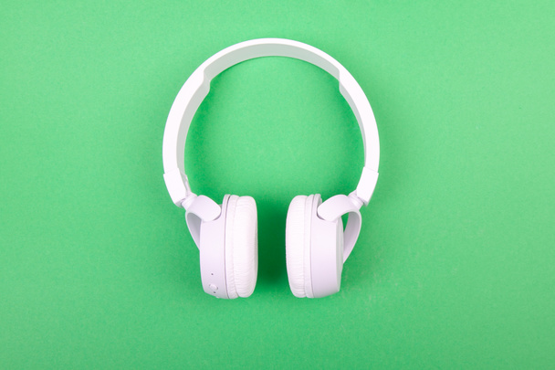Ασύρματα λευκά ακουστικά σε πράσινο φόντο. Μουσική έννοια. Ακουστικά σε πράσινο φόντο.  - Φωτογραφία, εικόνα