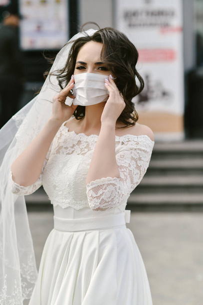 Bride in medical mask on street of city during coronavirus epidemic. Wedding day COVID-19 protection - Фото, изображение