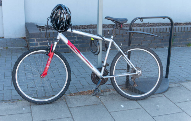 una vista de cerca de una bicicleta y un casco unidos a un poste con una cadena para evitar que sea robado mientras el propietario está en las tiendas
  - Foto, Imagen