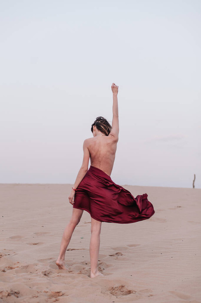 A girl with a fabric is standing in the wind in the desert - Photo, Image