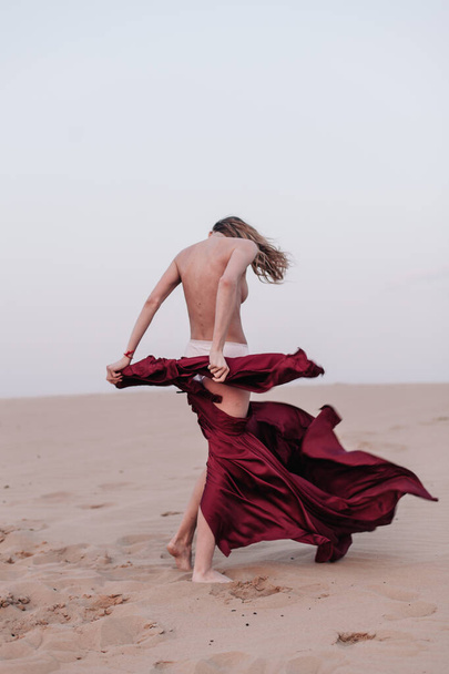 A girl with a fabric is standing in the wind in the desert - 写真・画像