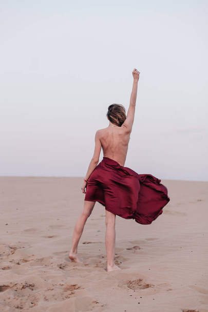 A girl with a fabric is standing in the wind in the desert - 写真・画像
