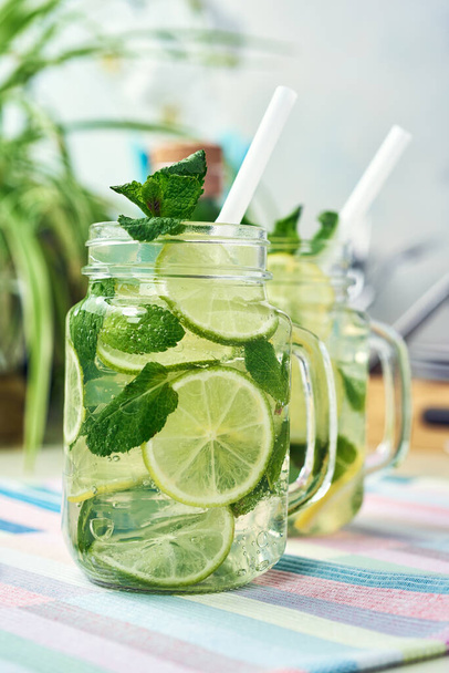 Two glasses of homemade lemon, lime, and mint lemonade sit on the wooden dining table. Cold, refreshing summer lemonade or mojito. - Fotoğraf, Görsel