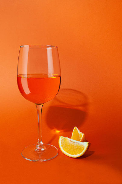 Cocktail aperol spritz. In a glass goblet. Next to the glass are two slices of orange. On a plain orange background. Hard light, sharp shadows. Close-up. Place for text. - Foto, afbeelding