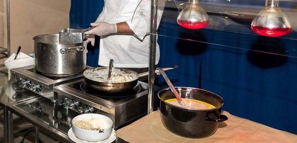 Chef bereitet Pasta während Brunch-Buffet oder Food-Blogger Konferenz oder Catering-Veranstaltung. Pasta-Station, warmes Essen, frische Pasta. Hände mit Handschuhen, Töpfen und Tellern auf Herd, Ofen, Live-Kochen - Foto, Bild