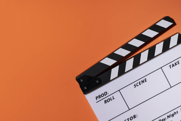 オレンジのテーブルを背景にした映画のクラッパー。映画、映画、ビデオ写真のコンセプト - 写真・画像