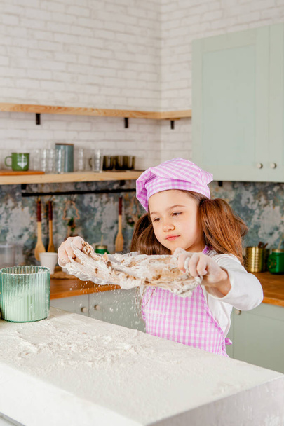 Mutfaktaki kız hamur yoğuruyor ve un serpiyor. - Fotoğraf, Görsel