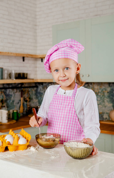Dziewczyna w kapeluszu szefa kuchni i fartuchu ugniata ciasto - Zdjęcie, obraz