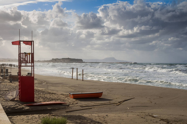 Playa de arena con una torre salvavidas y un bote rojo. No hay gente en otoño, durante un día lluvioso y tormentoso. Olas del mar y nubes intensas. Heraklion, Creta, Grecia
. - Foto, imagen
