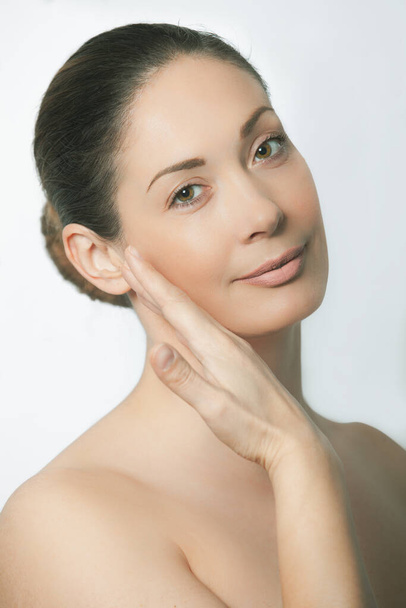 Beauty portrait of happy and positive woman. Natural face with small wrinkles, straight tied hair. Light white background. Hand near the face. Ideal for spa or wellness center. - Fotó, kép