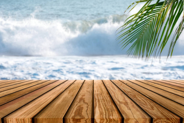 Bruin houten tafelblad op wazig golf spatten in tropische zee met palmblad achtergrond - Foto, afbeelding