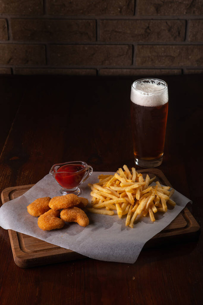 Nuggets french fries and sauce on a dark wooden background with beer - Фото, изображение