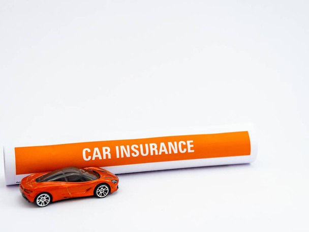 Hoge hoek schot van verzekeringspapier rol en een speelgoedauto op witte achtergrond met kopieerruimte - Foto, afbeelding