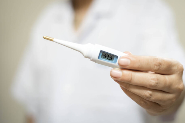 Une main de femme proche tient un thermomètre médical analogique pour mesurer la température corporelle, la protection contre le virus, la grippe et les maladies respiratoires. Coronavirus COVID-19 concept
. - Photo, image