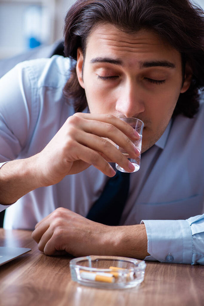 Mužský zaměstnanec pije vodku a kouří cigarety na pracovišti - Fotografie, Obrázek