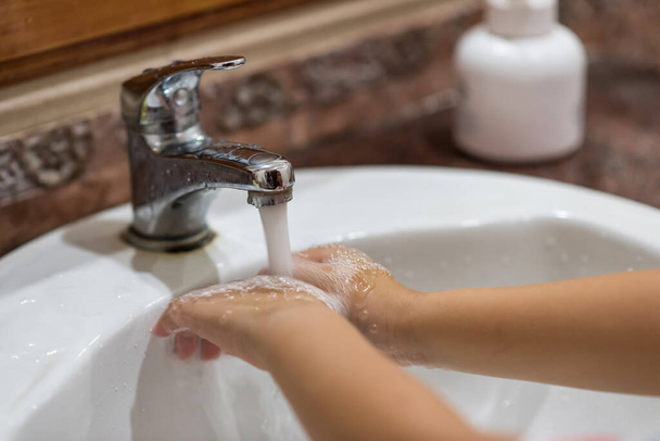 Мальчик моет руки, промывая мыло водой в раковине. Препарат covid-19, сделанный вручную. Защита от пандемии, чтобы остановить коронавирус. Оставайтесь дома, карантин, социальное дистанцирование
. - Фото, изображение