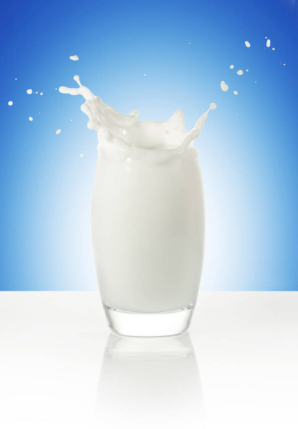 melk spatten in een glas geïsoleerd op blauwe achtergrond - Foto, afbeelding