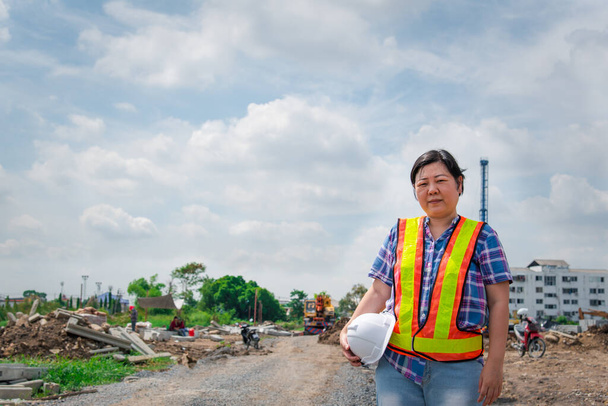 Azji kobieta inżynier budownictwa lub architekt z kasku i kamizelki bezpieczeństwa szczęśliwy pracując w budynku lub na placu budowy - Zdjęcie, obraz