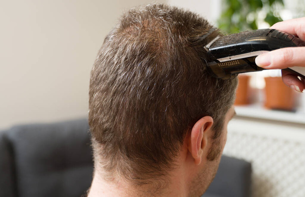 Woman is doing haircut with hair trimmer to man at home. - Photo, Image