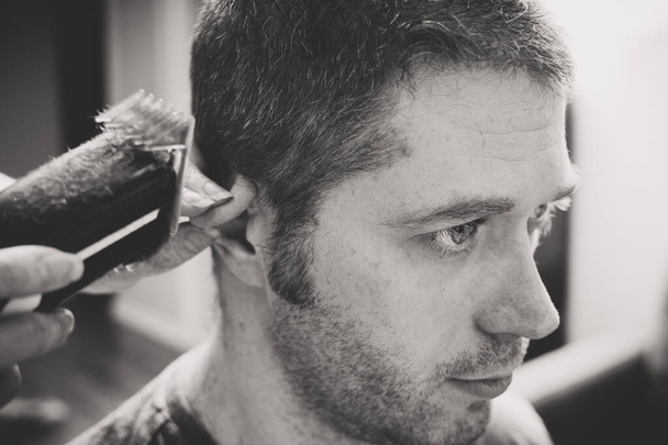 Donna sta facendo taglio di capelli con tagliacapelli per l'uomo a casa. Foto in bianco e nero
. - Foto, immagini