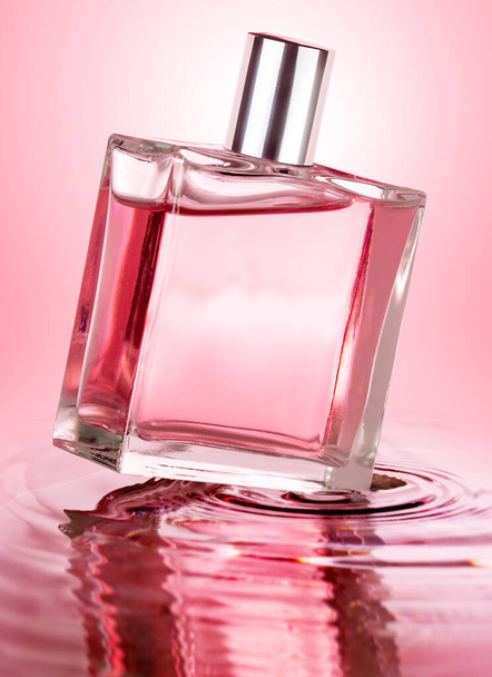 ピンクの背景に隔離された波打つ水の上に香水瓶 - 写真・画像