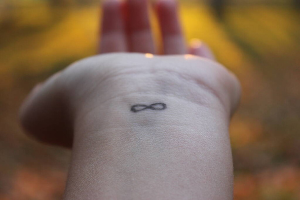 close-up van de arm met een infinity symbool getatoeëerd in zijn pols. Oneindigheidsteken op de hand. eindeloze liefde concept - Foto, afbeelding