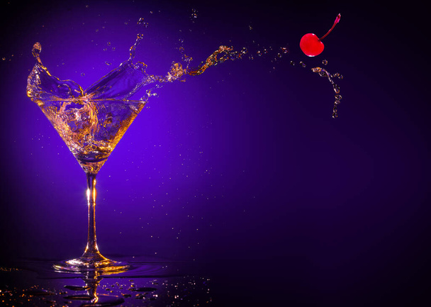 piros cseresznye fröccsenő ki egy martini pohár lila alapon - Fotó, kép