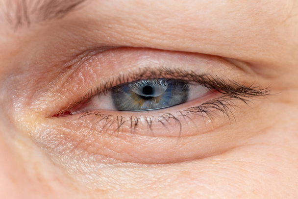 Женщина средних лет сузила сине-серый глазной макрос. Кавказская этническая принадлежность
. - Фото, изображение