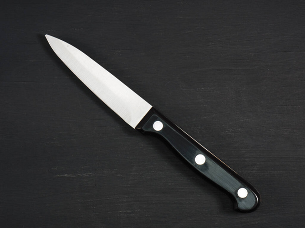 Medium sharp kitchen knife with black handle on a black wooden board. Healthy eating, recipe concept - Фото, зображення