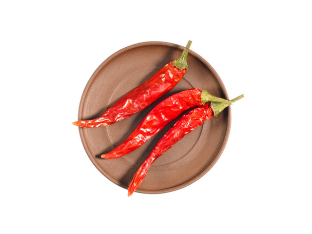 Spice red pepper chili pods on brown clay plate isolated on white. Healthy eating, ayurveda, naturopathy concept - 写真・画像