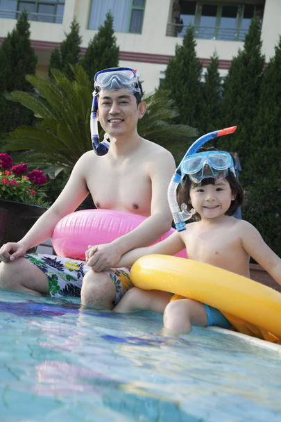 Батько і син сидять біля краю басейну
 - Фото, зображення