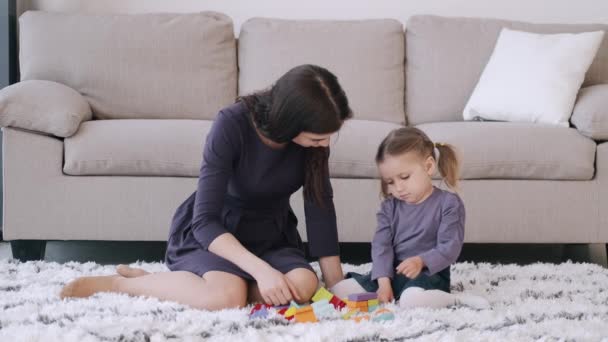 Beautiful mother and toddler daughter are playing construction toys together in a room - Video
