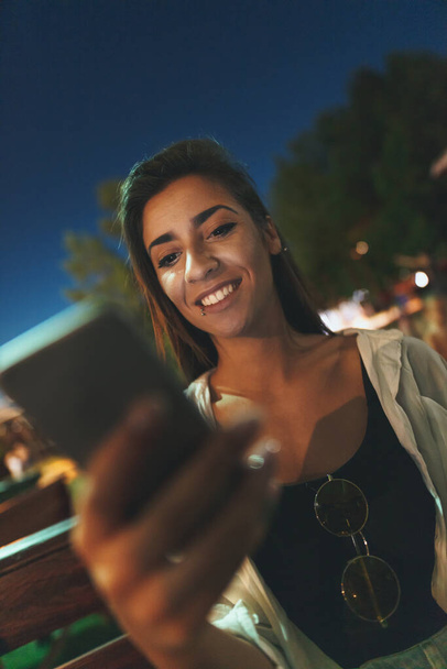 Mladý pěkný úsměv žena surfování síť s smartphonem v letním večeru.  - Fotografie, Obrázek