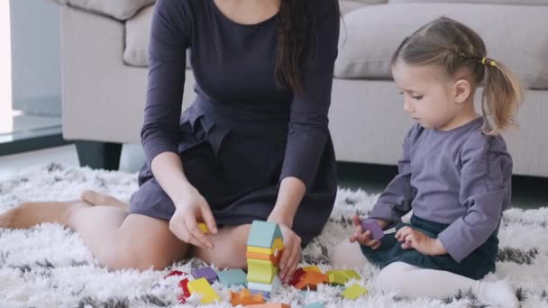 Beautiful mother and toddler daughter are playing construction toys together in a room - Video, Çekim