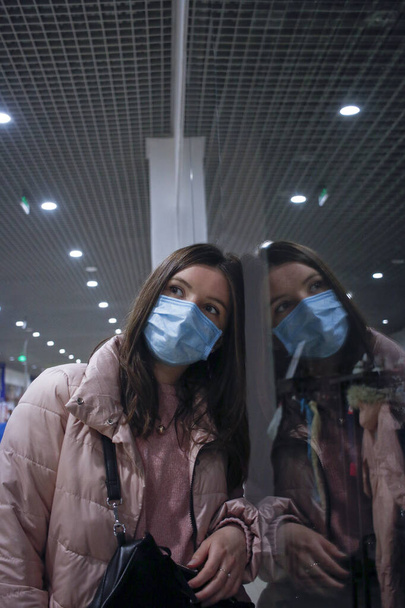 meisje alleen in medisch masker reflecteren in het glas - Foto, afbeelding