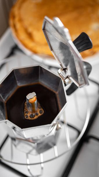 Kahvi valmistautuu moka potin pannukakkuja taustalla. Kahvin valmistus käyttäen italialaista vedenkeitintä ruostumattomasta teräksestä
 - Valokuva, kuva