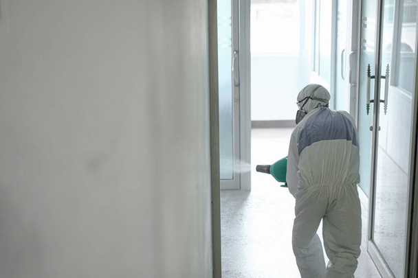 Desinfecção de escritório para evitar COVID-19, pessoa em terno branco hazmat com desinfetar no escritório, trabalhador desinfetante usar máscara protetora e naipe sprays coronavírus
. - Foto, Imagem