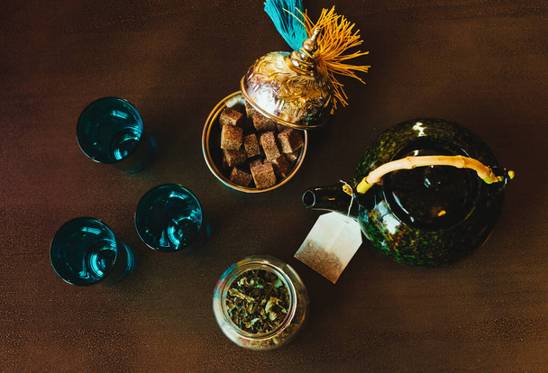 Théière, sucre, verres à thé et menthe sur une table brune
 - Photo, image